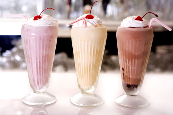 tre bicchieri a righe verticali con milk shake, panna montata e una ciliegia